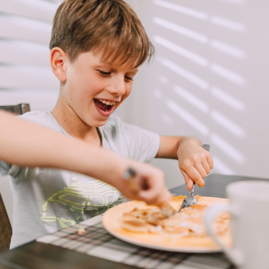 kid cuts into pancake while sitting at table 